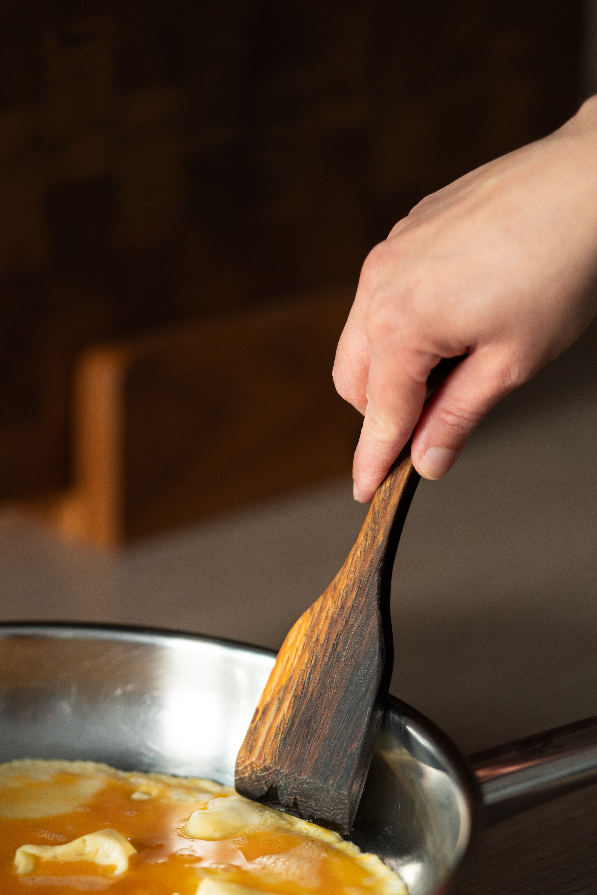 Pfannenwender aus Holz beim Kochen in einer Pfanne mit warmer Werkstattatmosphäre